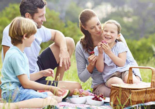 Parents outdoors on a sunny day enjoying a picnic with their kids.